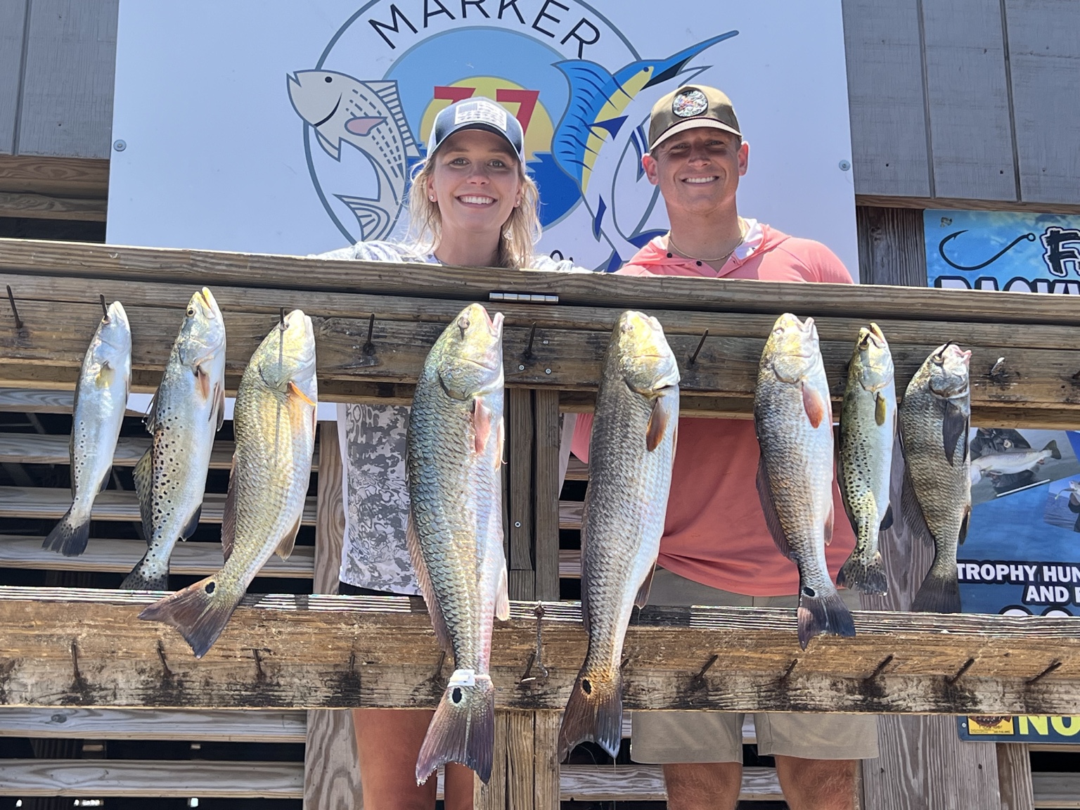 Two anglers behind a rack of redfish and speckled trout at Marker 37
