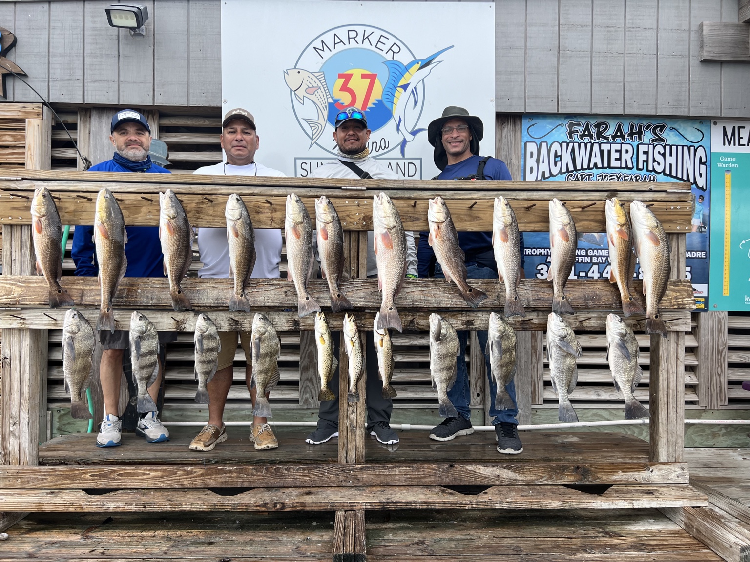 Four anglers behind a full rack of redfish, black drum, and speckled trout at Marker 37