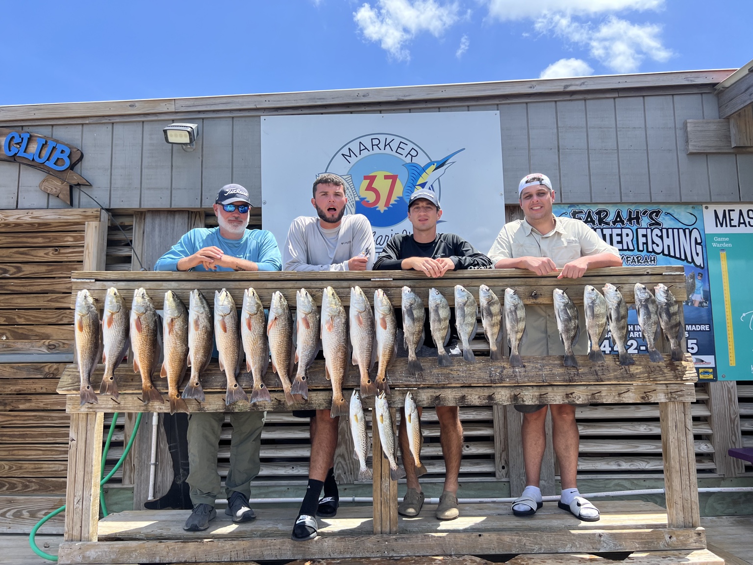 Four anglers behind a rack of redfish and speckled trout at Marker 37