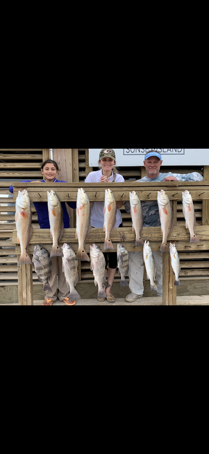 Three anglers behind a full rack of redfish, black drum, and speckled trout at Sunset Island