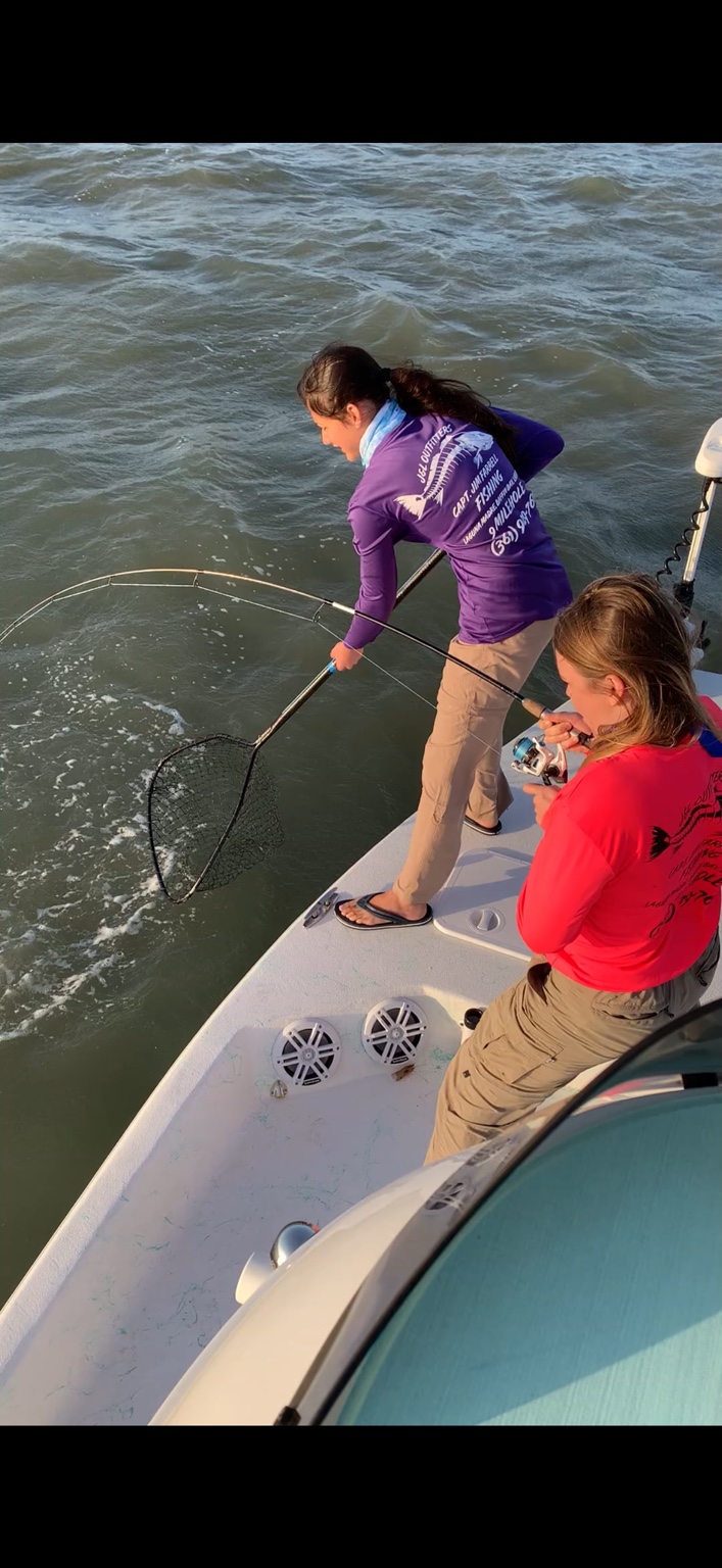 Angler fighting a redfish while another angler works the landing net
