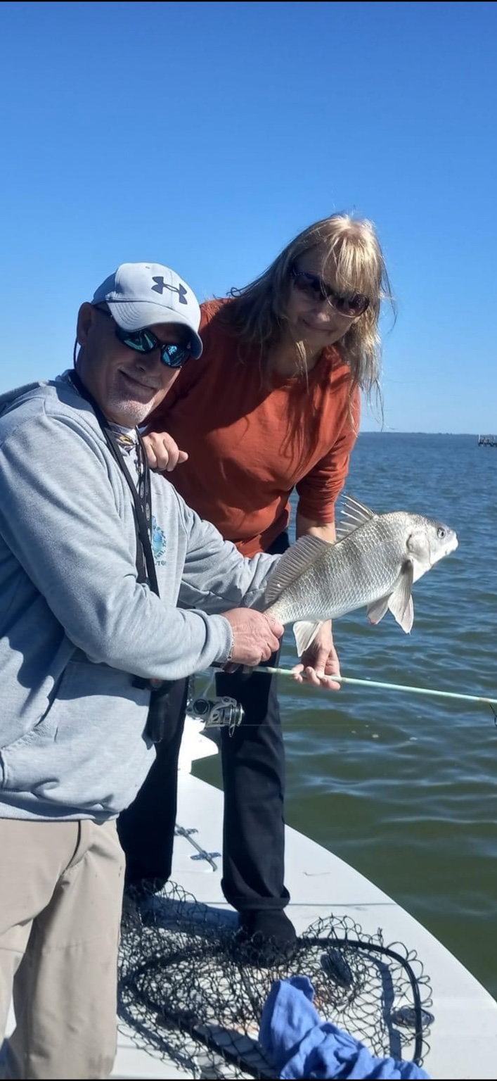 Two anglers holding a black drum on the boat