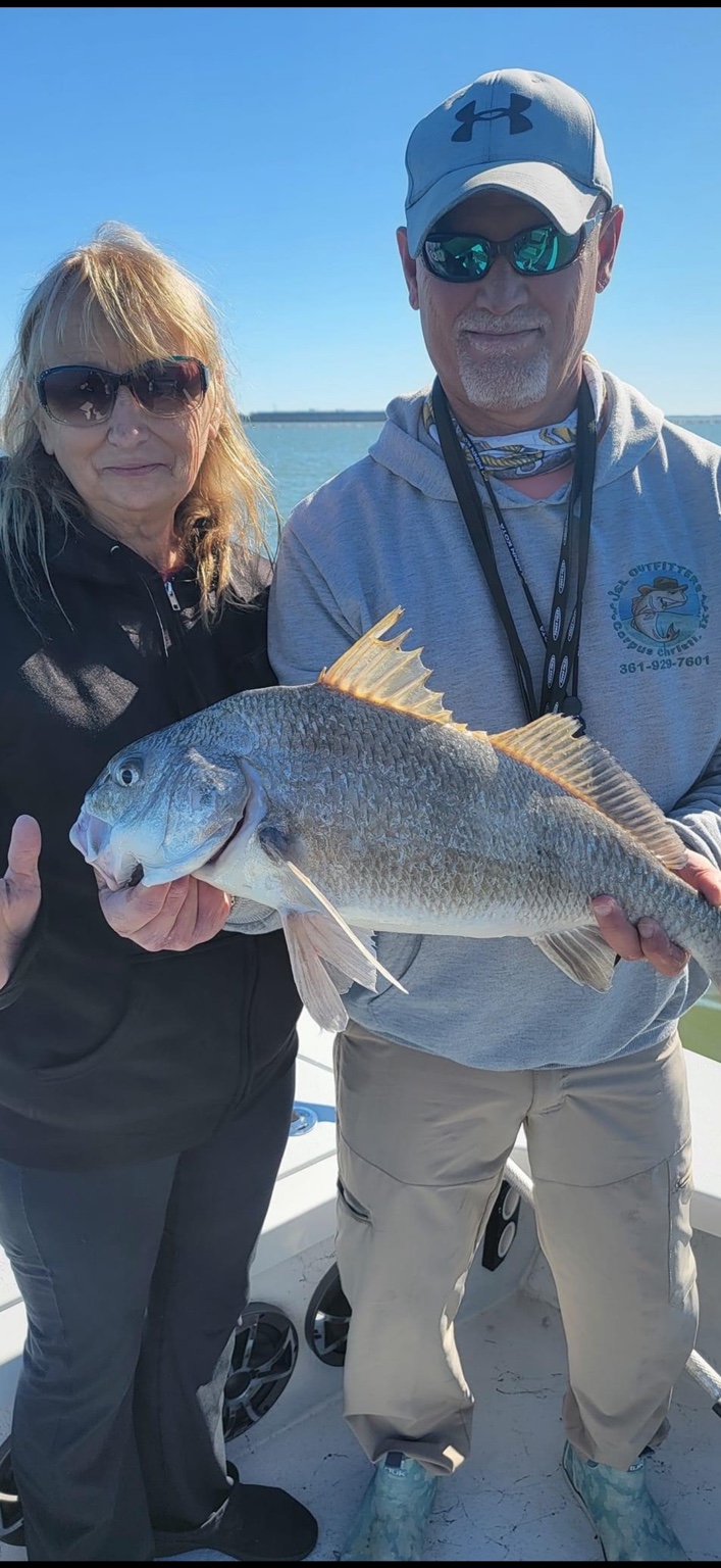 Two anglers holding a large black drum on the boat