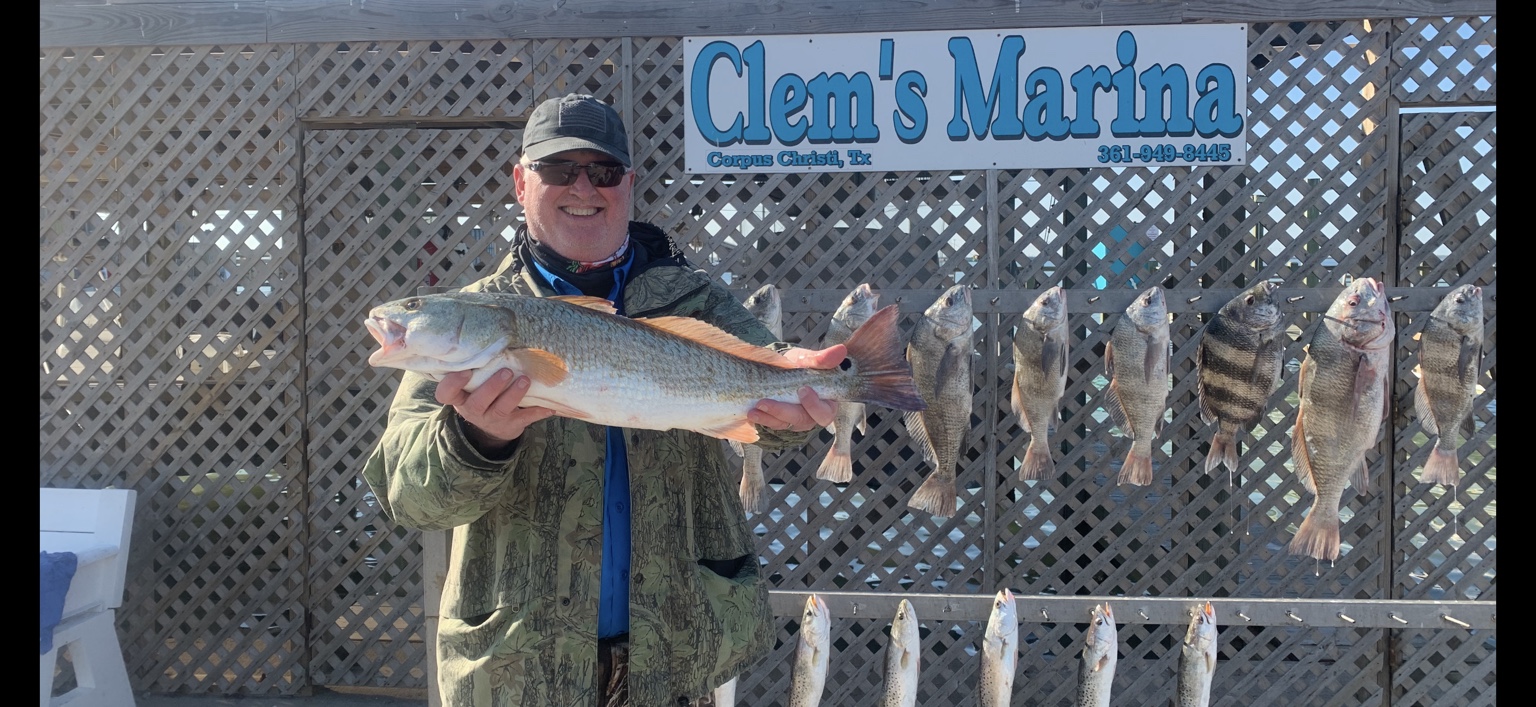 Angler holding a large redfish in front of a full fish rack at Clem's Marina