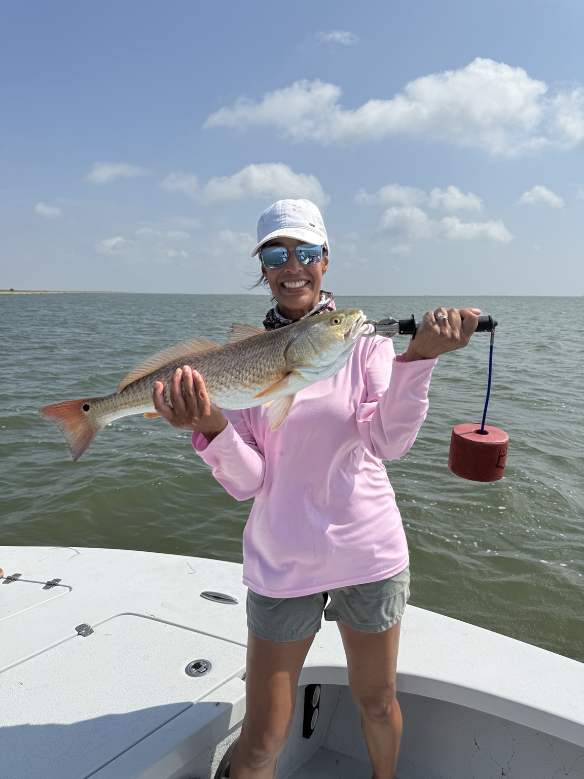 Woman in a pink fishing shirt holding a redfish on the boat